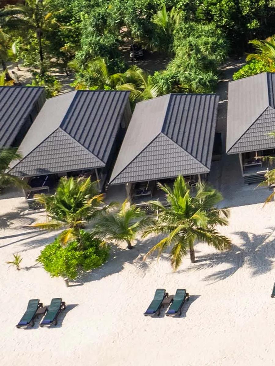 O Beach Villa exterior, a dark wood cottage with a private terrace under palm trees