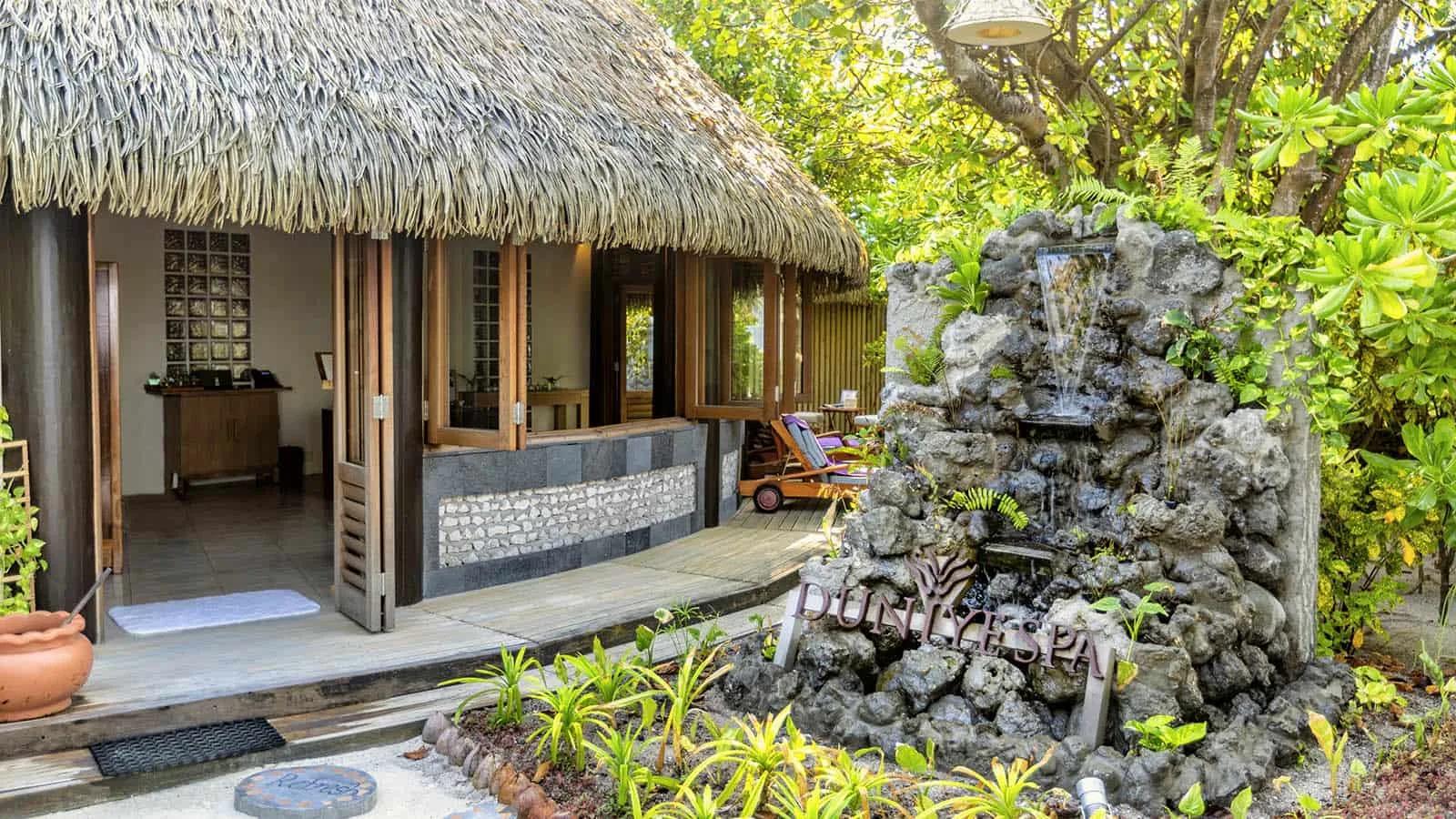 The entrance to Duniye Spa, its thatched roof beside a rock-cut water feature set among the trees
