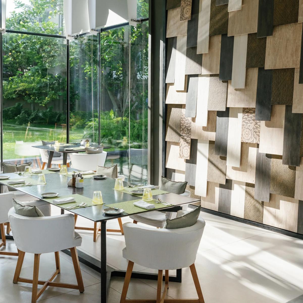 The White's dining room, tables set beneath a geometric wood-shingle wall with floor-to-ceiling windows onto the garden