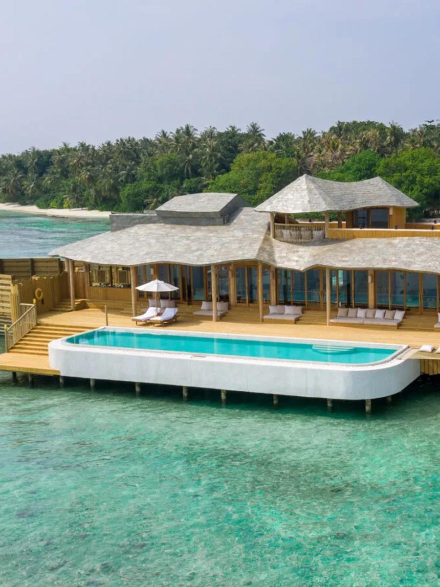 A 2-Bedroom Water Reserve with Slide, its white pool built out over the reef with a slide curving down into the lagoon and the island's beach visible behind