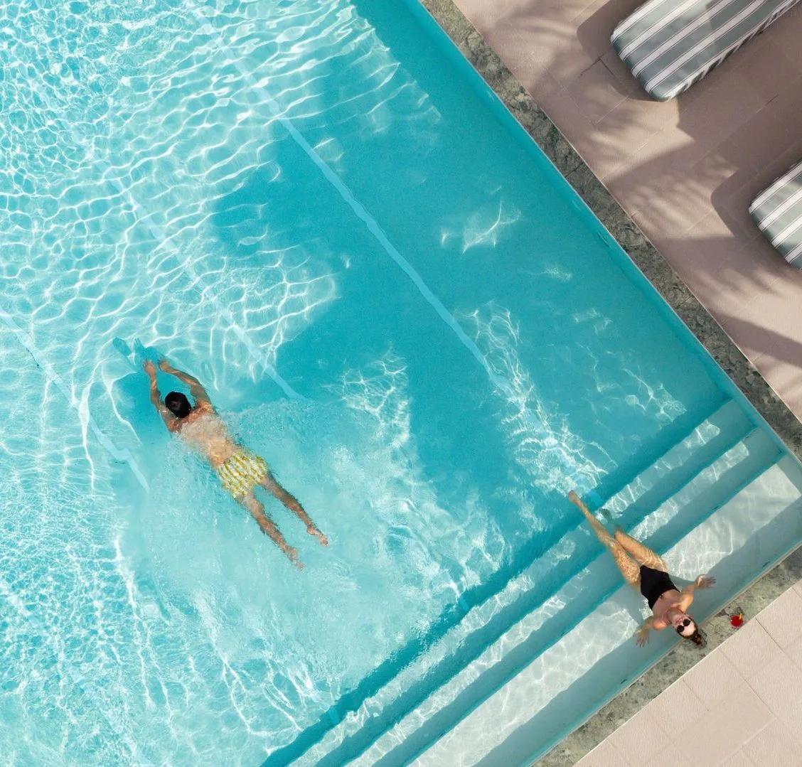 A guest swimming in the infinity pool at West Beach Bar, OBLU SELECT Lobigili, loungers on the deck alongside