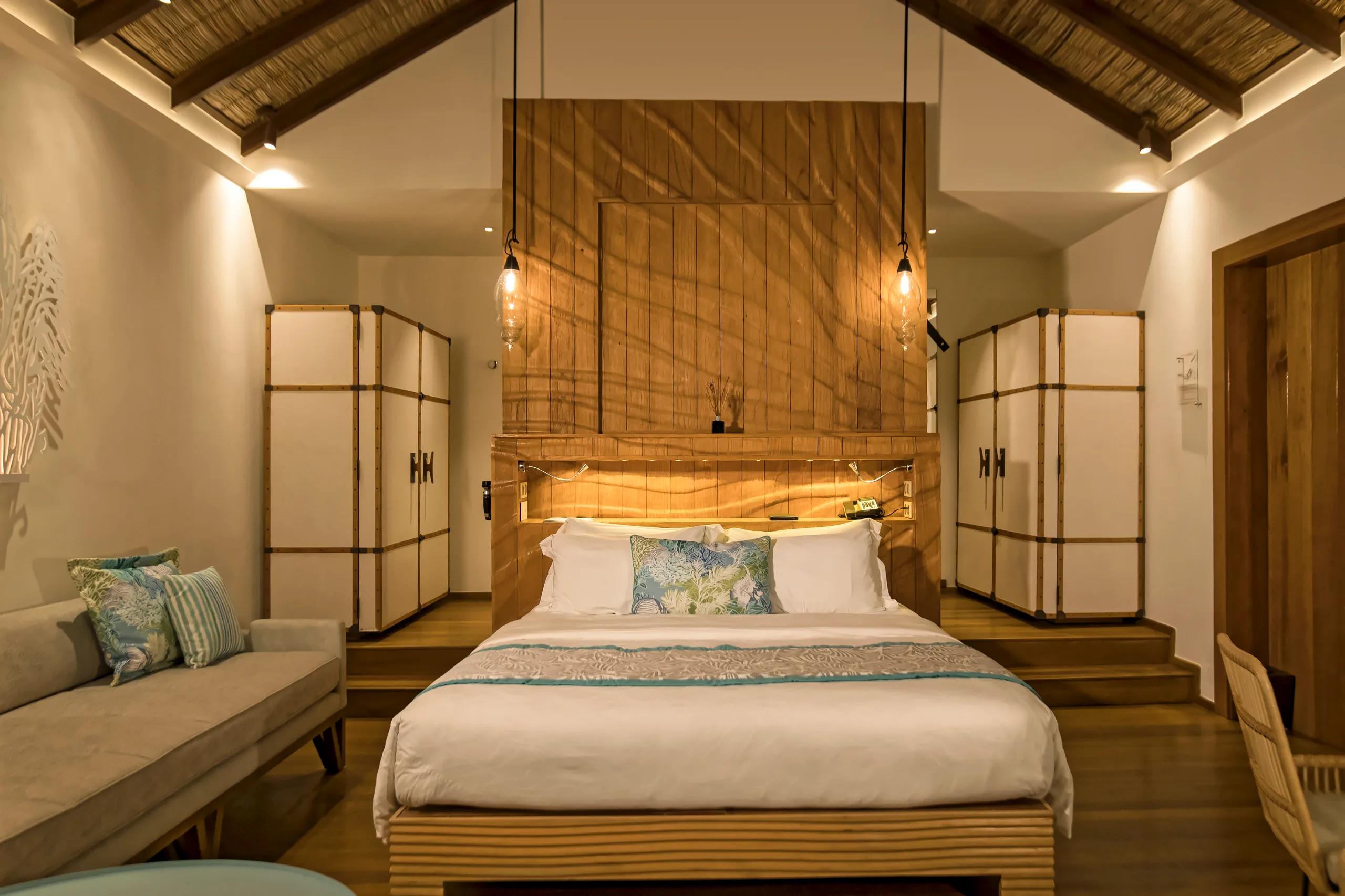 Interior of a Water Villa bedroom with sofa seating, thatched ceiling, and sliding doors open to the lagoon