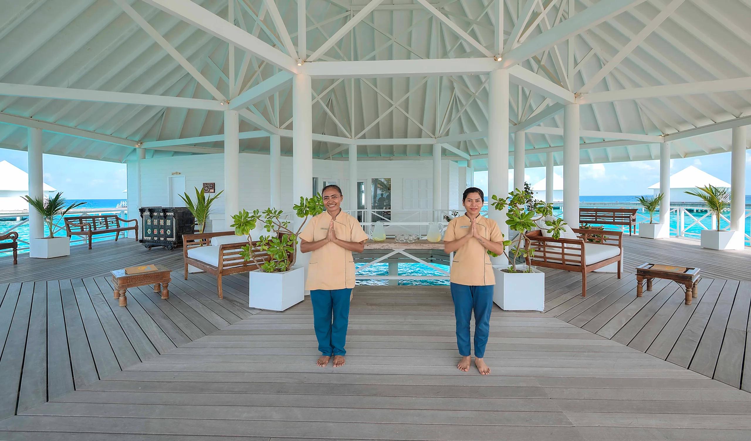 Two Serena Spa therapists greeting guests with a traditional gesture on the spa's overwater lounge deck