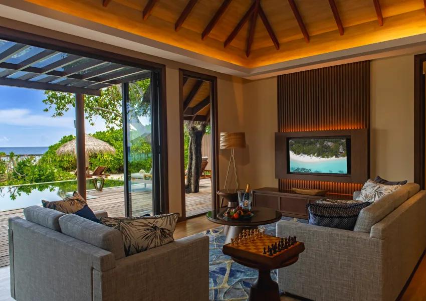 The wood-panelled living room of the Two-bedroom Baros Retreat, opening through sliding doors onto its private pool deck and garden
