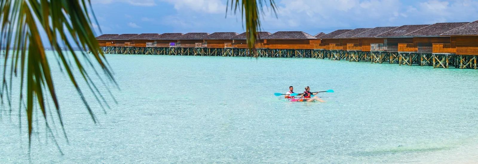 Two kayakers paddling across the lagoon in front of Vilamendhoo's overwater villas