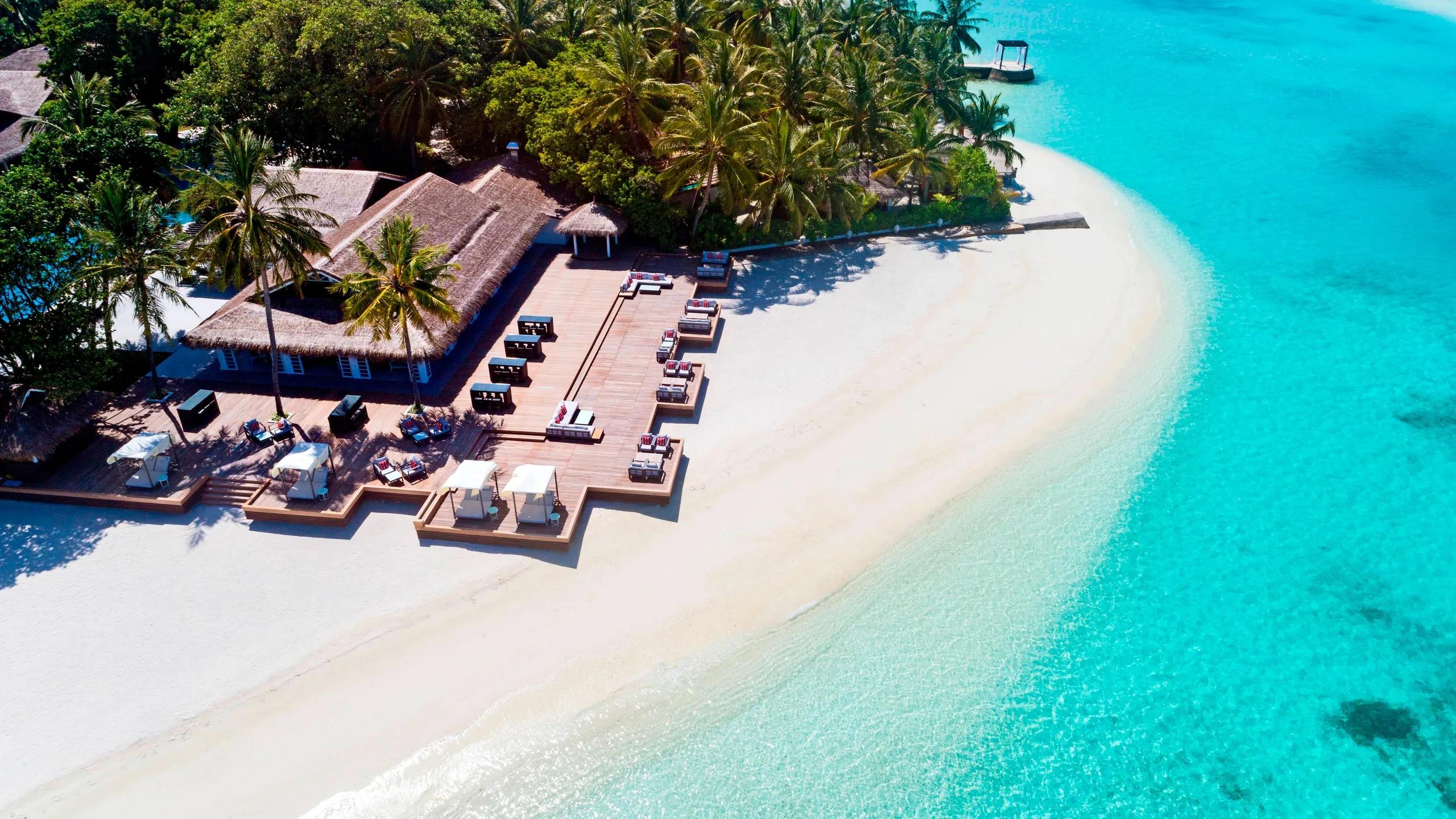 Aerial view of Anchorage's beachfront deck, sun loungers and a thatched pavilion set where the island narrows toward the lagoon