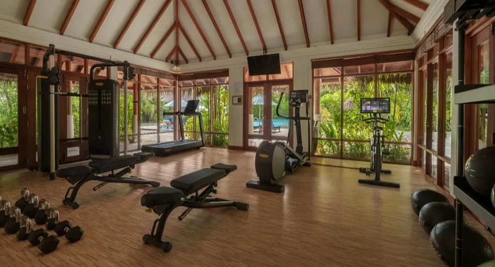 An air-conditioned gym with free weights, cardio machines and floor-to-ceiling windows looking onto tropical gardens and a pool