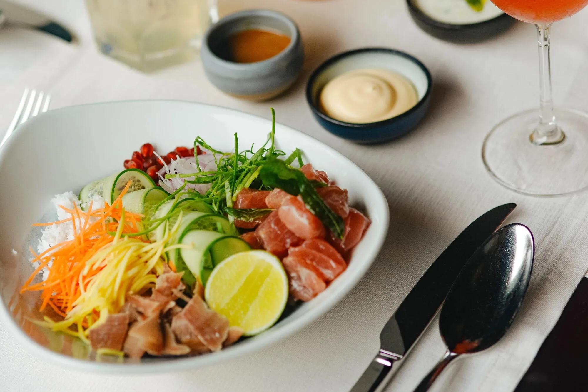 A tuna poke bowl with pickled vegetables, lime and dipping sauces, plated at Mura Bar