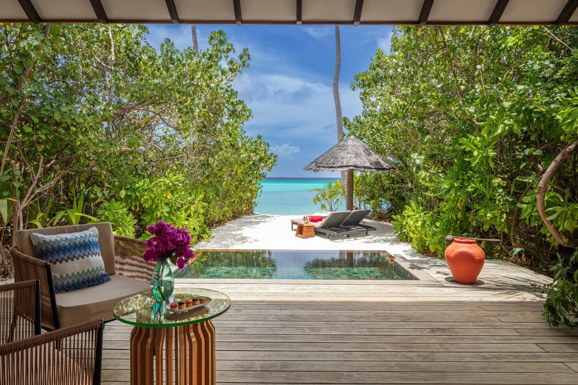 A Sunset Beach Pool Villa's terrace and private pool, loungers and a thatched umbrella set on white sand with the open sea ahead
