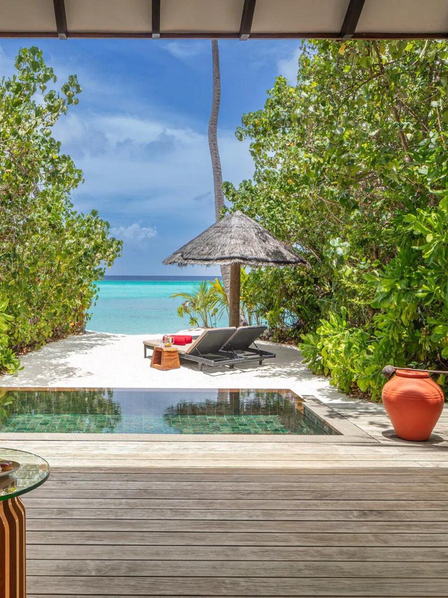 A Sunset Beach Pool Villa's terrace and private pool, loungers and a thatched umbrella set on white sand with the open sea ahead