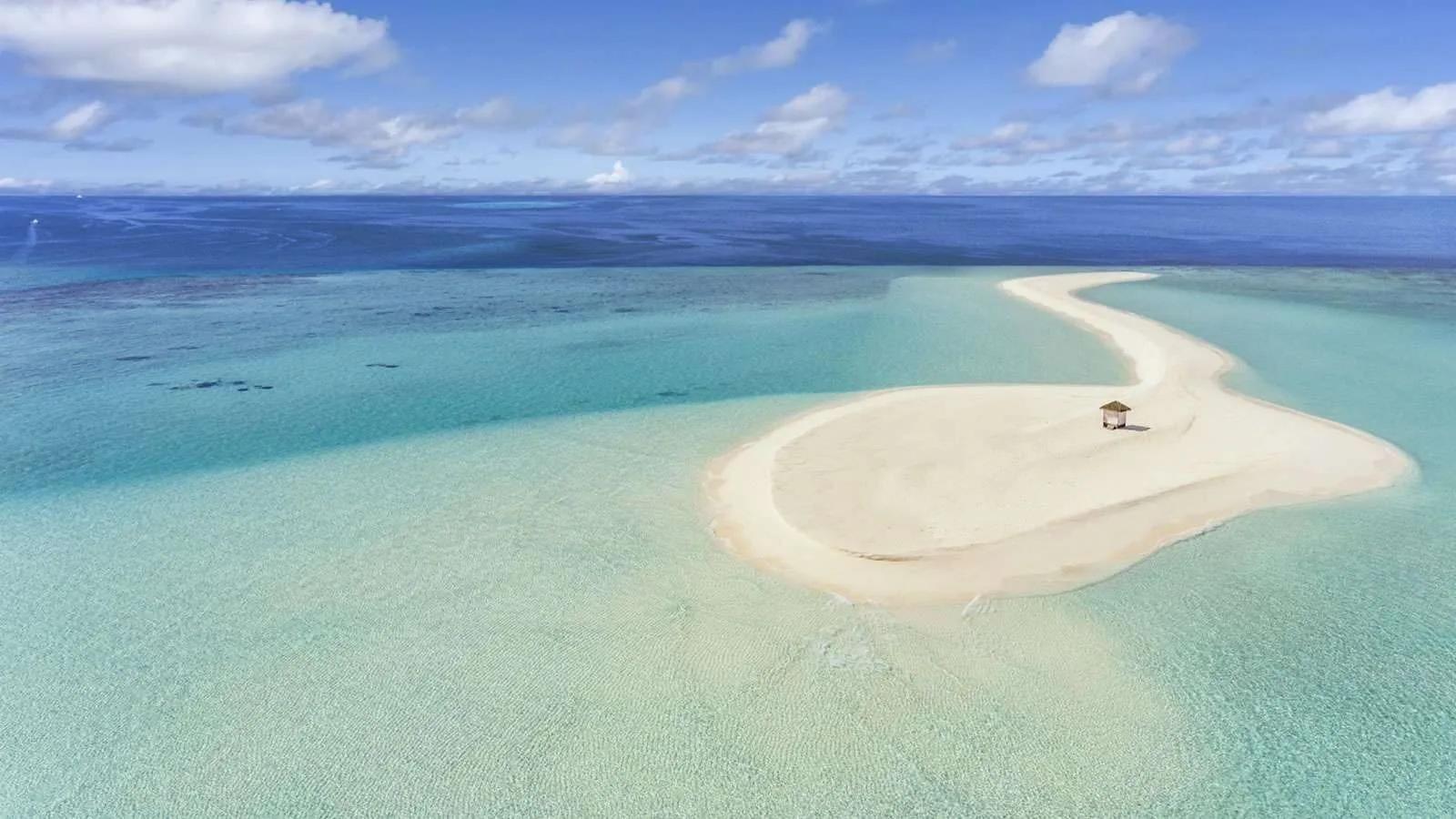 A single thatched hut on an isolated sandbank ringed by shallow turquoise water