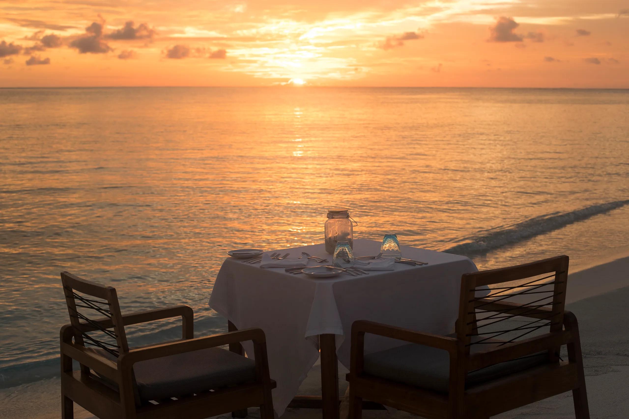 A candlelit table for two set directly on the sand at sunset, waves breaking a few metres away