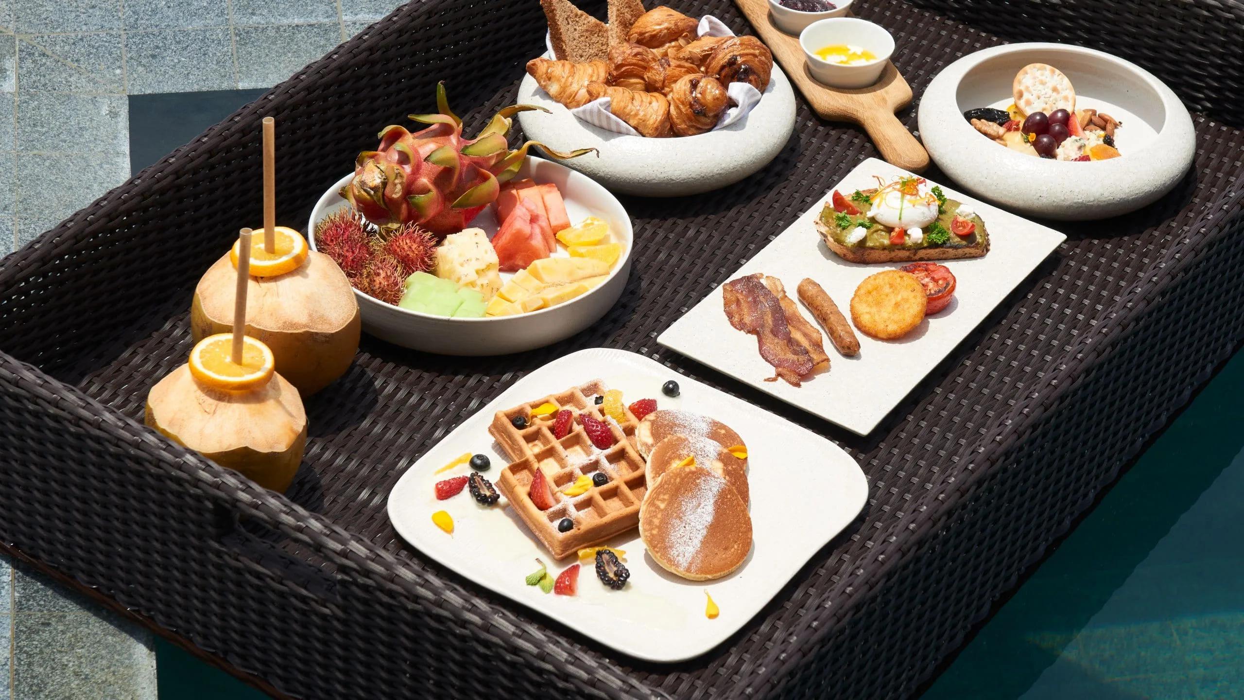 A floating breakfast spread of pastries and fruit set on a tray across a villa's private pool