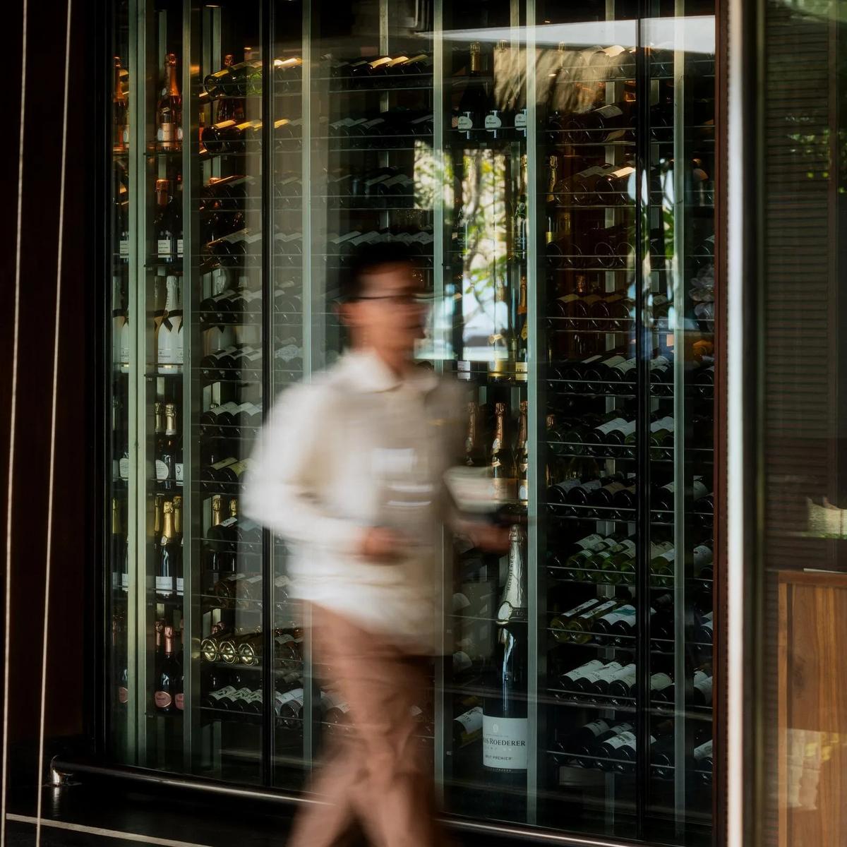 A staff member walks past Reethi's glass-walled wine cellar at One&Only Reethi Rah, carrying a bottle of champagne