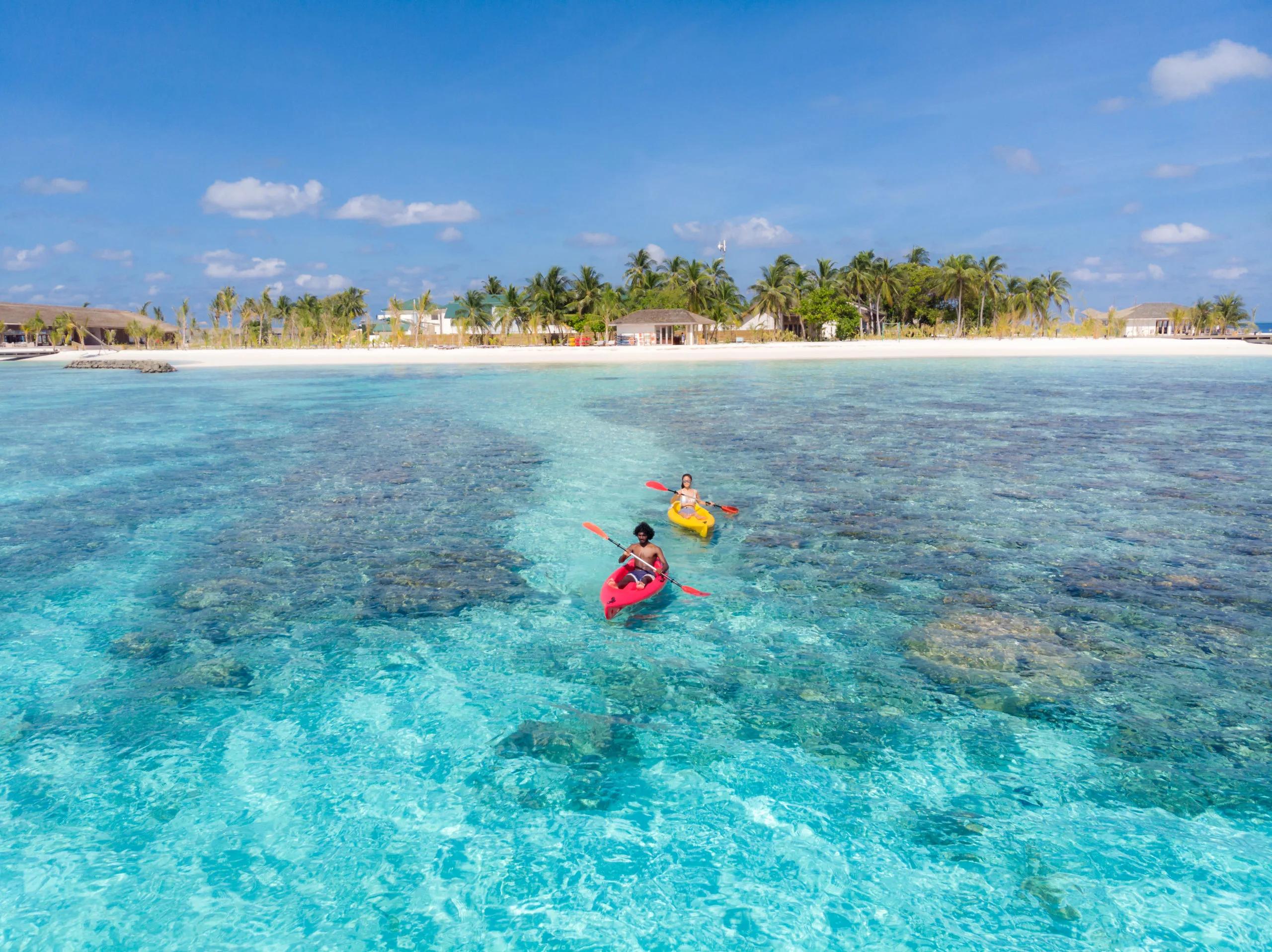 An aerial view of two guests kayaking over Kagi's house reef, coral formations visible through the clear water