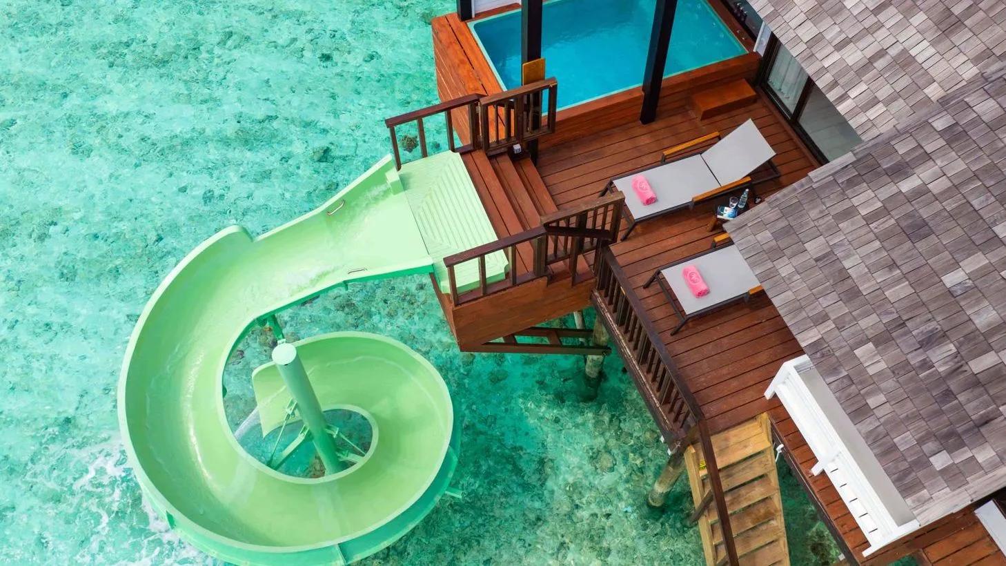 Aerial view of a green spiral water slide curling from an overwater deck into the lagoon