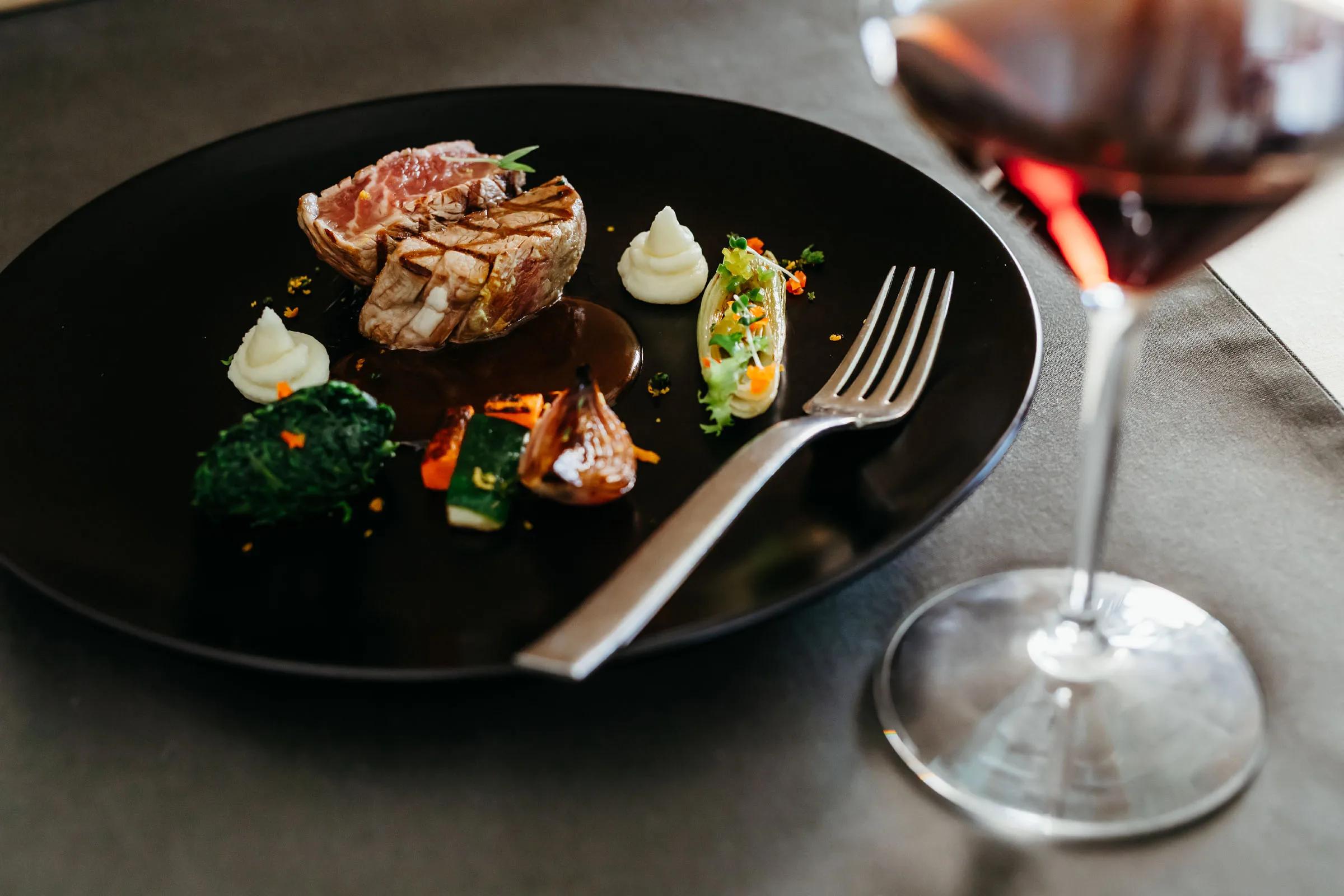 A finely plated seared dish with vegetables beside a glass of red wine, from Flavours' French menu