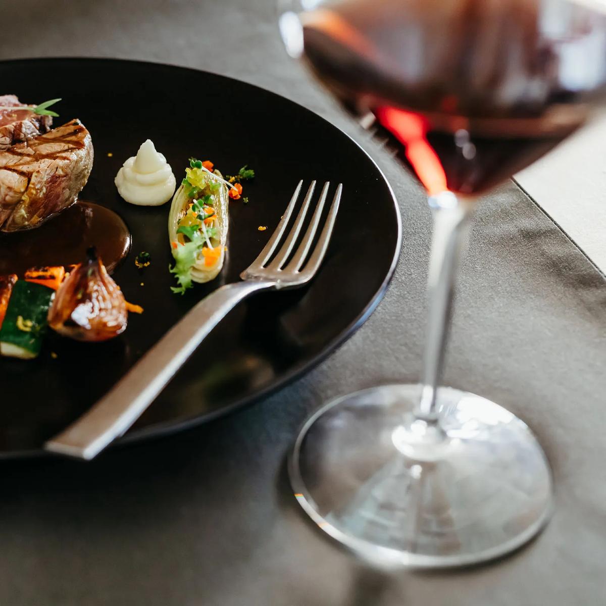 A finely plated seared dish with vegetables beside a glass of red wine, from Flavours' French menu