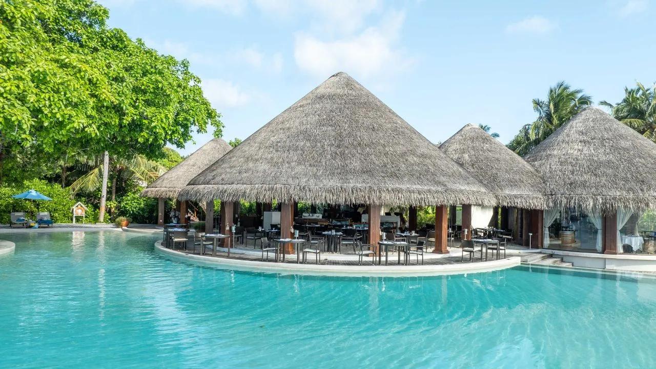 Sea Grill's open-air dining deck ringed by Dusit Thani Maldives' infinity pool, thatched roofs and palm trees behind