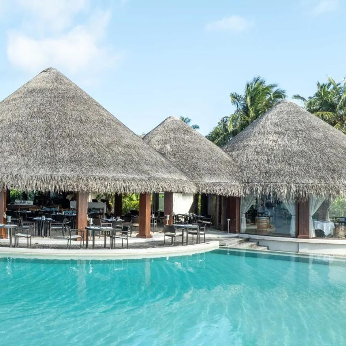 Sea Grill's open-air poolside dining deck at Dusit Thani Maldives, thatched roofs and palm trees surrounding the infinity pool
