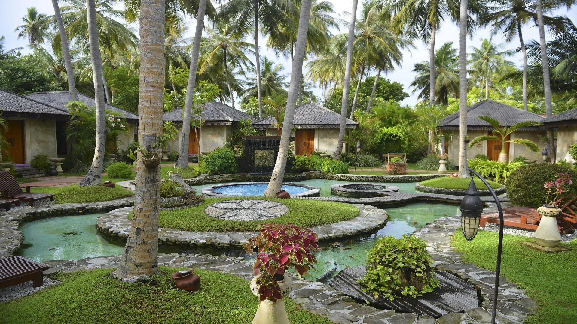 The garden grounds of Orchid Spa at Bandos, thatched treatment pavilions set among tall palms and ornamental ponds