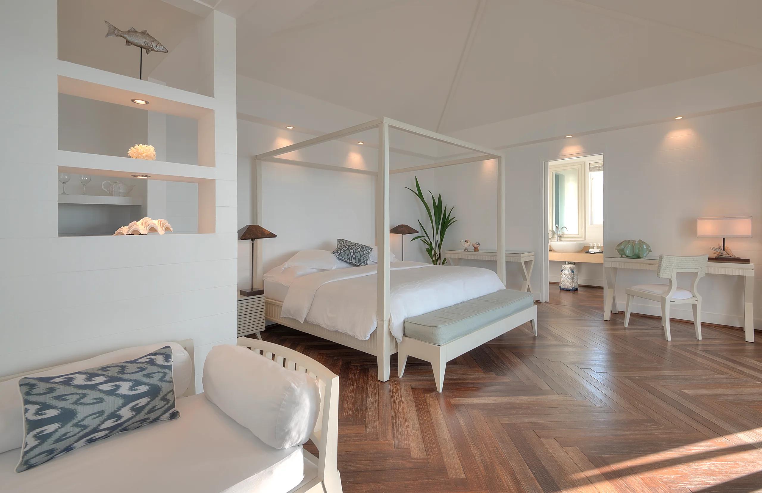 A One Bedroom Water Villa's four-poster bed, with the living area and ensuite visible beyond