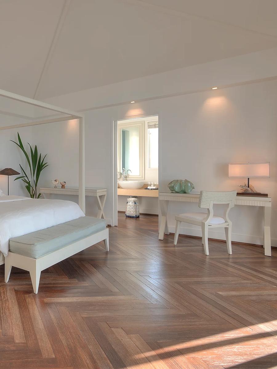 A One Bedroom Water Villa's four-poster bed, with the living area and ensuite visible beyond