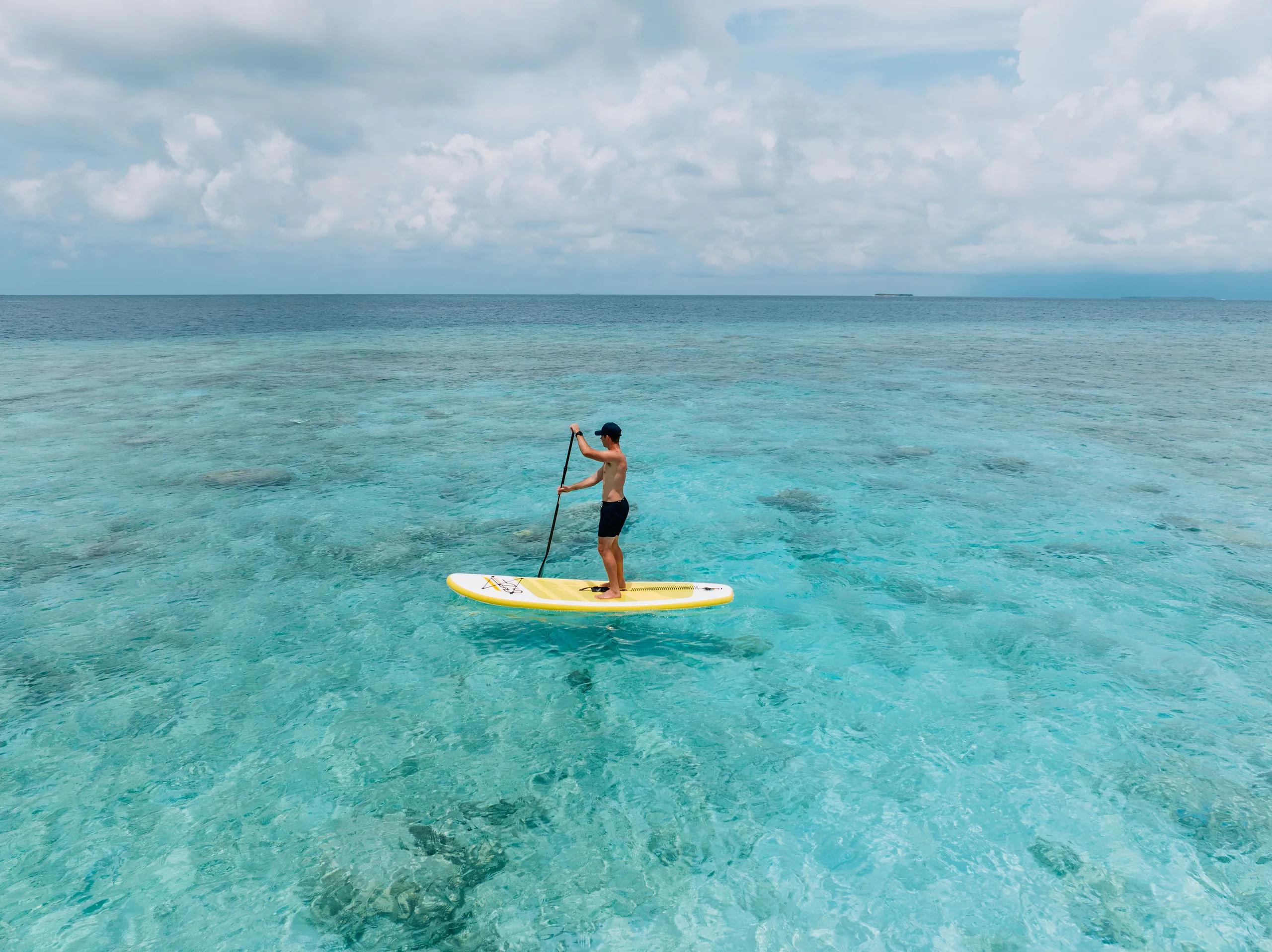 A guest paddleboarding across the clear, shallow lagoon off Diamonds Thudufushi
