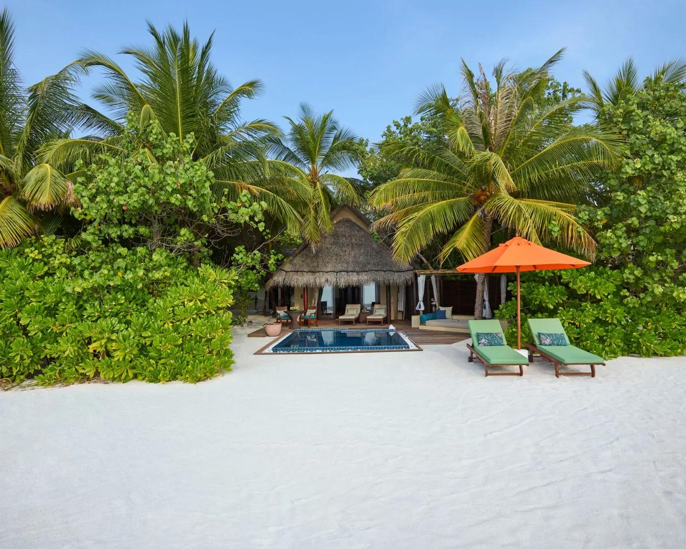A Sunset Beach Villa with Pool seen from the beach, palm trees framing its private pool and thatched roof