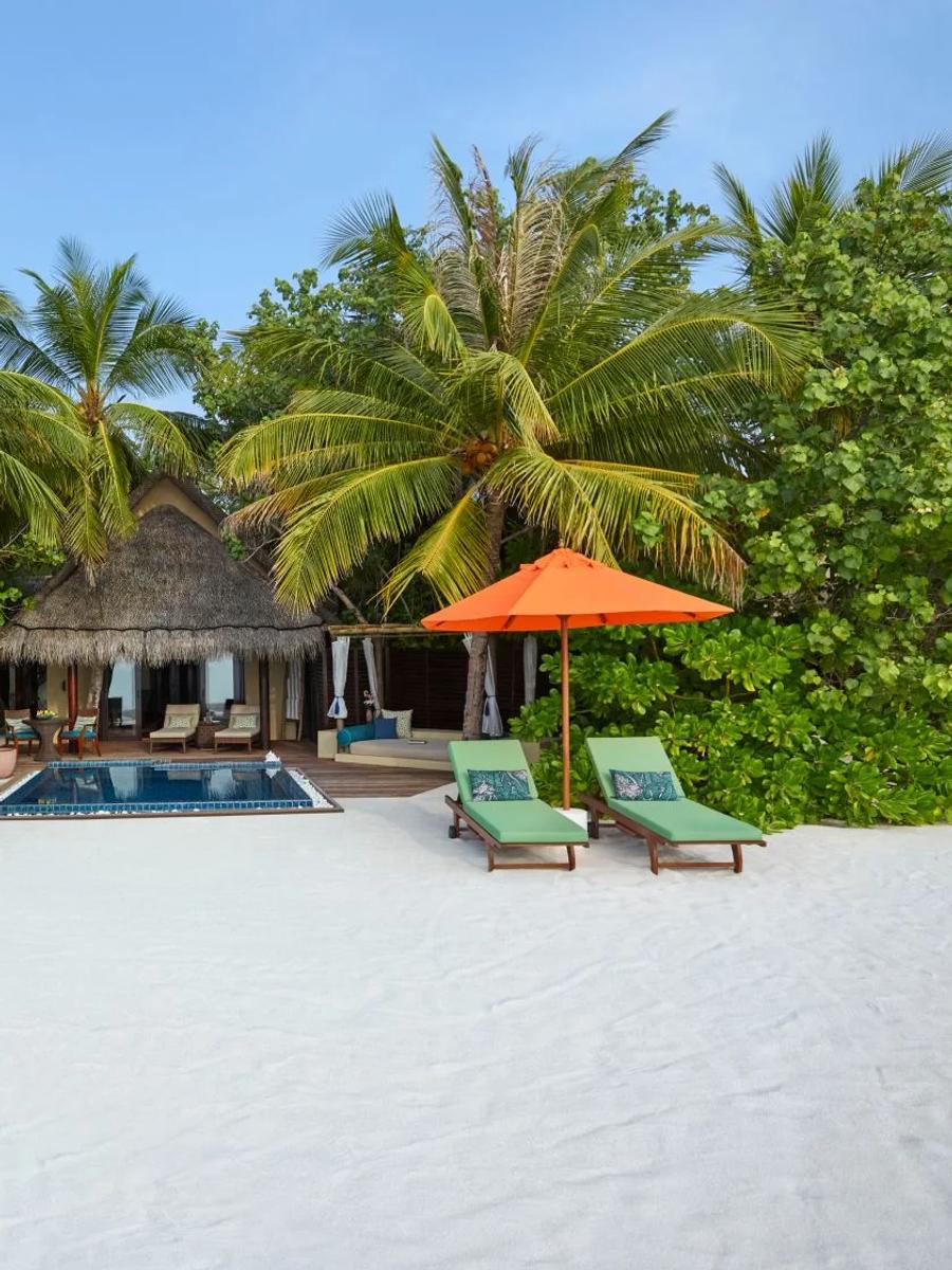 A Sunset Beach Villa with Pool seen from the beach, palm trees framing its private pool and thatched roof