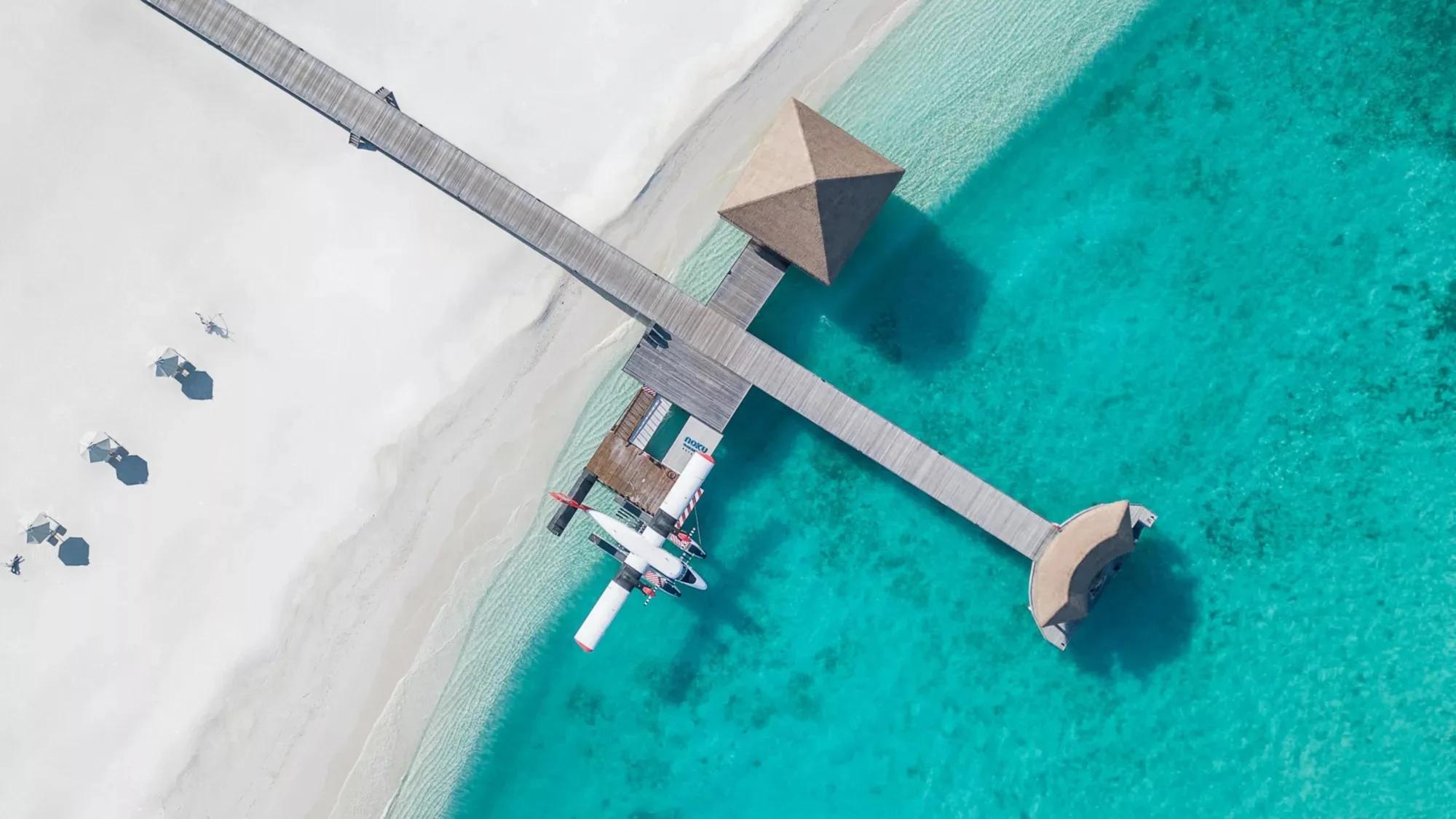 A seaplane docked at Noku Maldives' overwater jetty, turquoise reef water on both sides