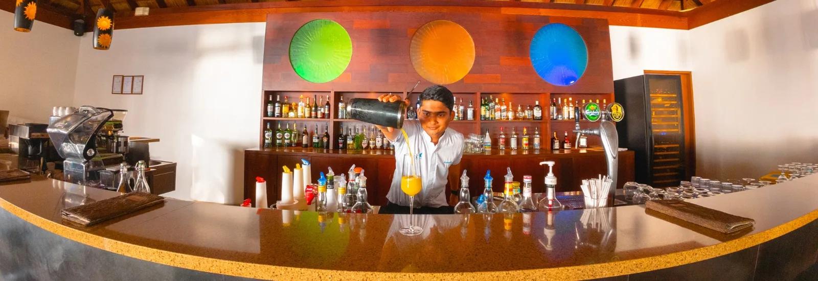 A bartender preparing a cocktail behind the counter at Sunset Bar