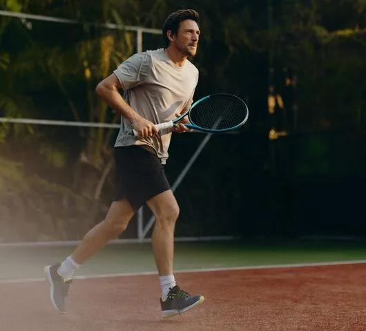 A man mid-swing on JOALI's tennis court, racquet drawn back, palms lining the court