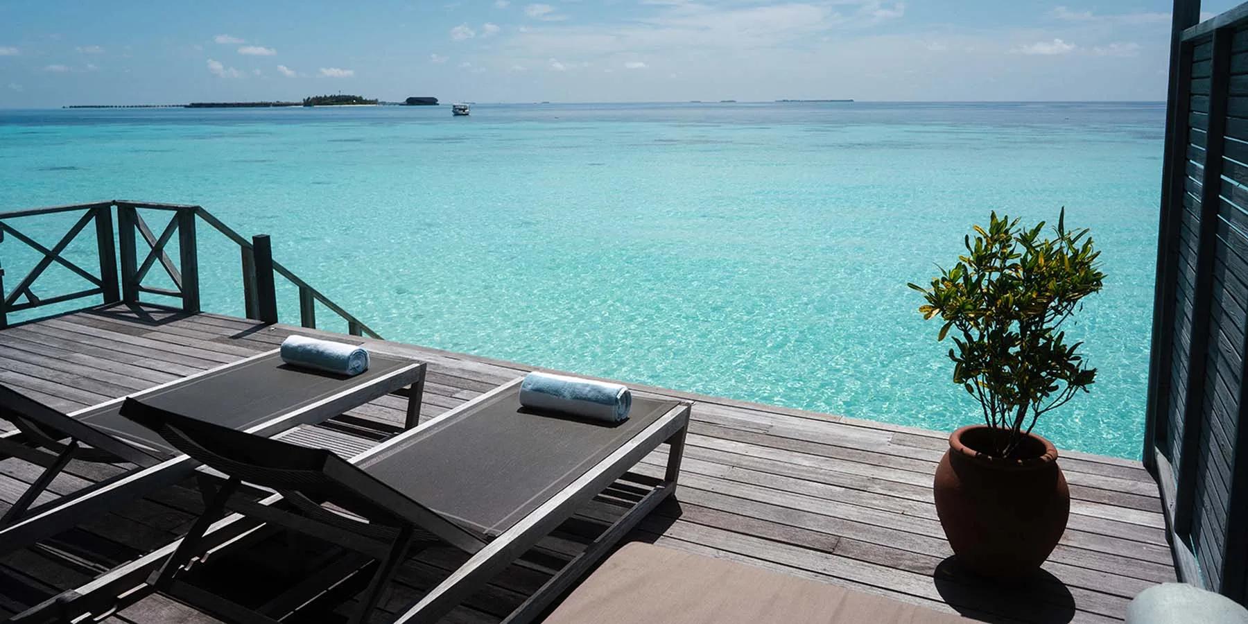 The deck of a Jacuzzi Water Villa, sun loungers facing an open lagoon view toward the horizon