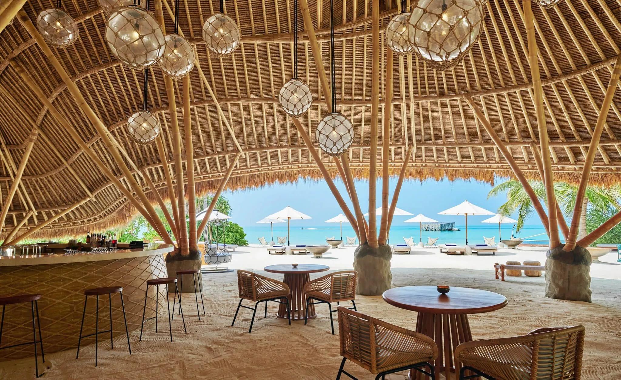 Interior view of Onu Onu's domed bamboo roof with hanging glass pendant lights, bar counter to one side and the beach and lagoon visible beyond the open sides