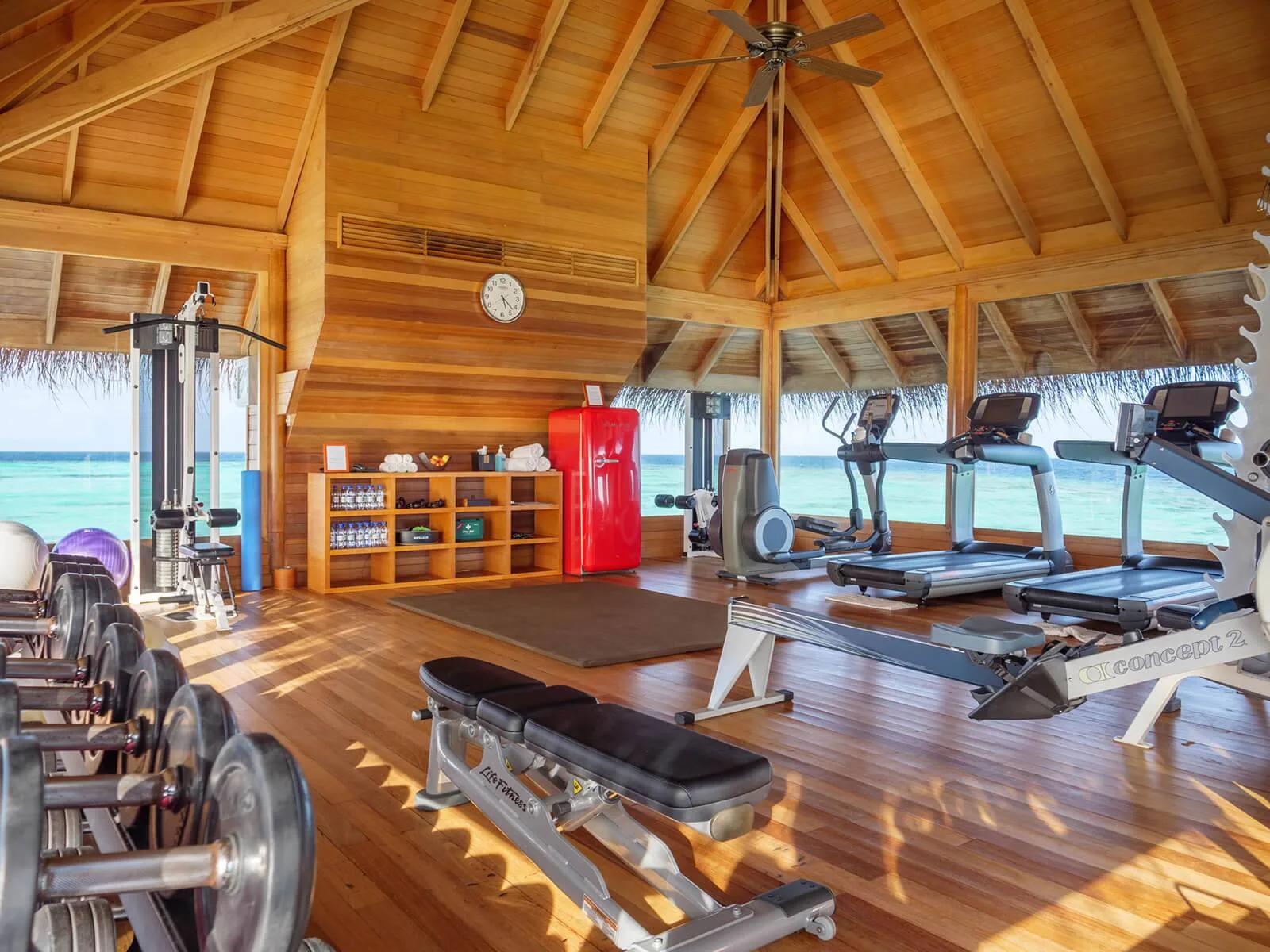 Treadmills and free weights lined up facing the lagoon inside Huvafen Fushi's overwater gymnasium