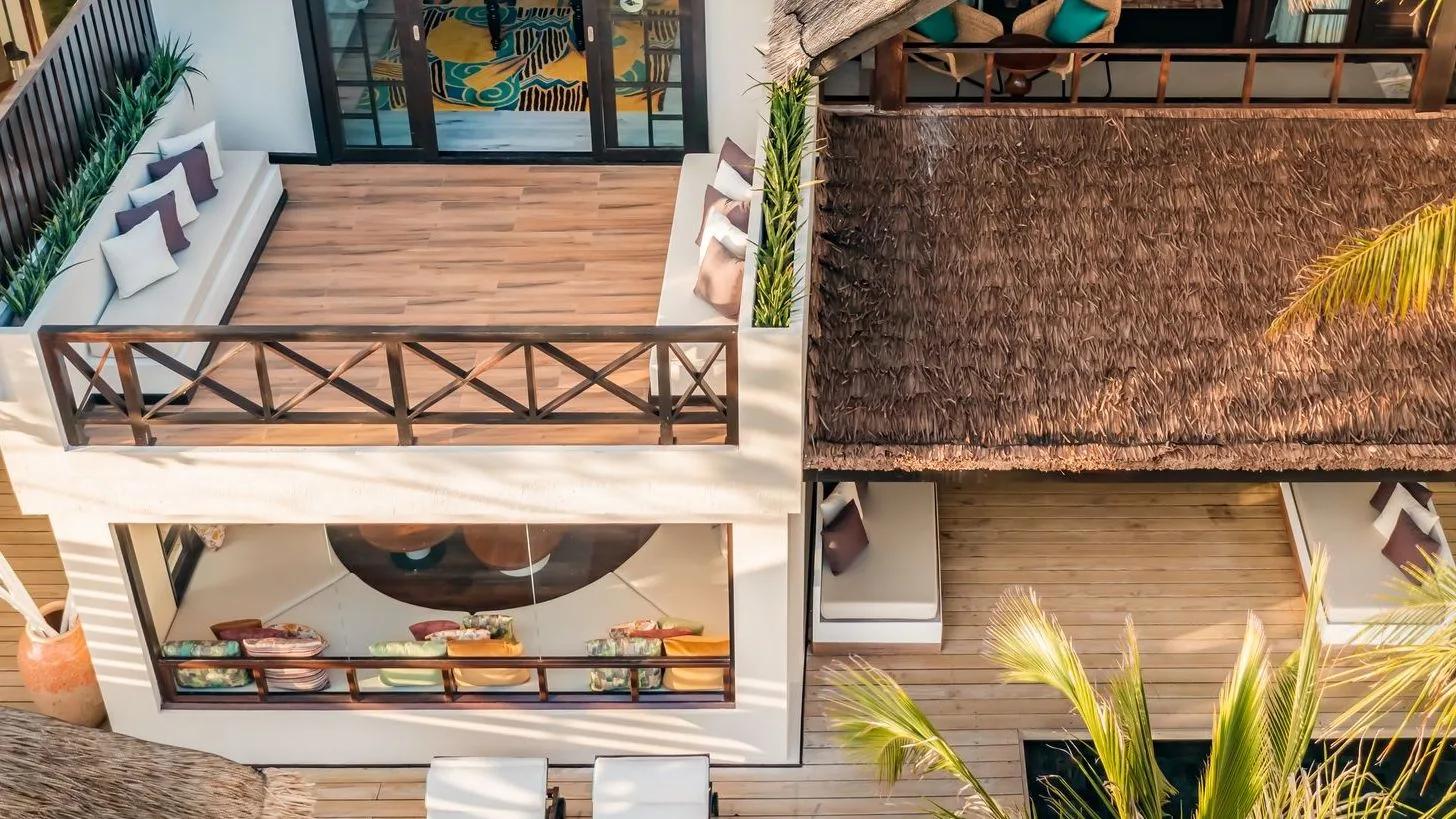 A bedroom's sliding glass doors opening onto a sand path through tropical planting toward the villa's outdoor dining pavilion