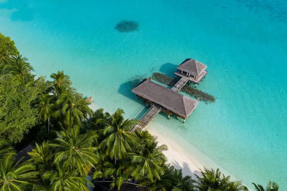 Aerial view of Lime Wellbeing's overwater treatment pavilion, connected to the island by a wooden jetty over the lagoon