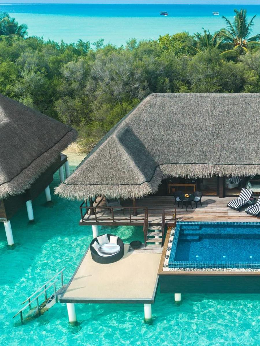 An aerial view of a One Bedroom Sunrise Overwater Suite with Pool, a guest relaxing on a lounger beside its private pool