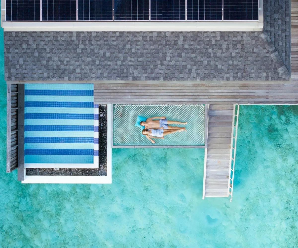 Aerial view of a couple lying on an overwater hammock beside a striped plunge pool at SO/ Maldives