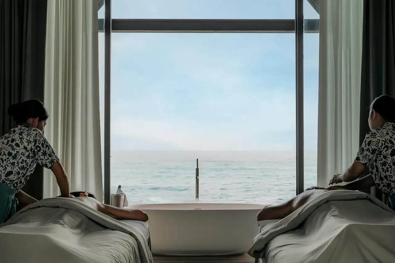 A couple's treatment room at Veyoge Spa, with an ocean-view soaking tub between the massage beds