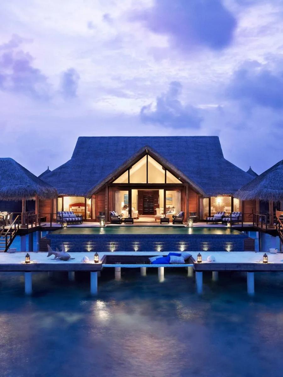 The Rehendhi Presidential Suite at dusk, its symmetrical thatched pavilions lit warmly over the lagoon