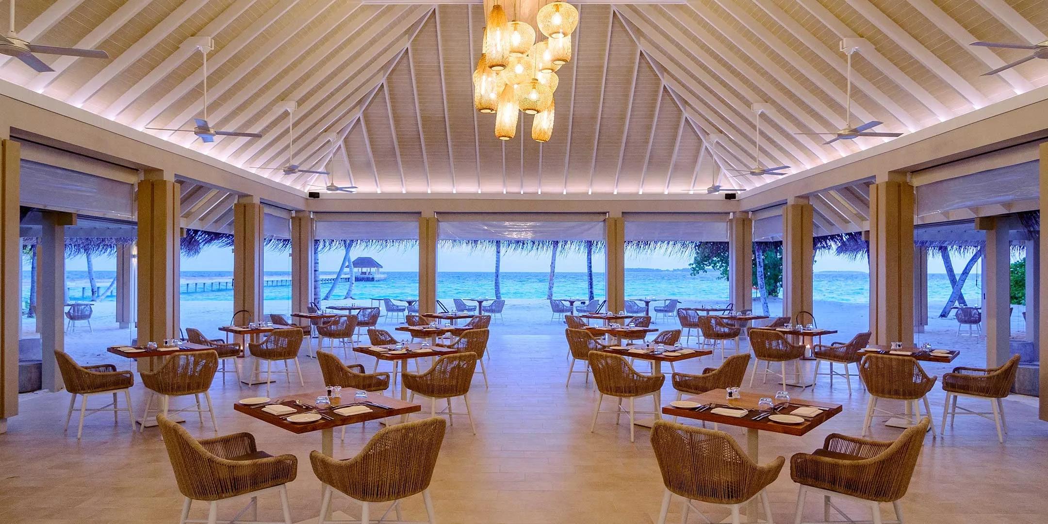 Taste's open-air dining pavilion set with tables for dinner, palm trees and the lagoon visible beyond the columns