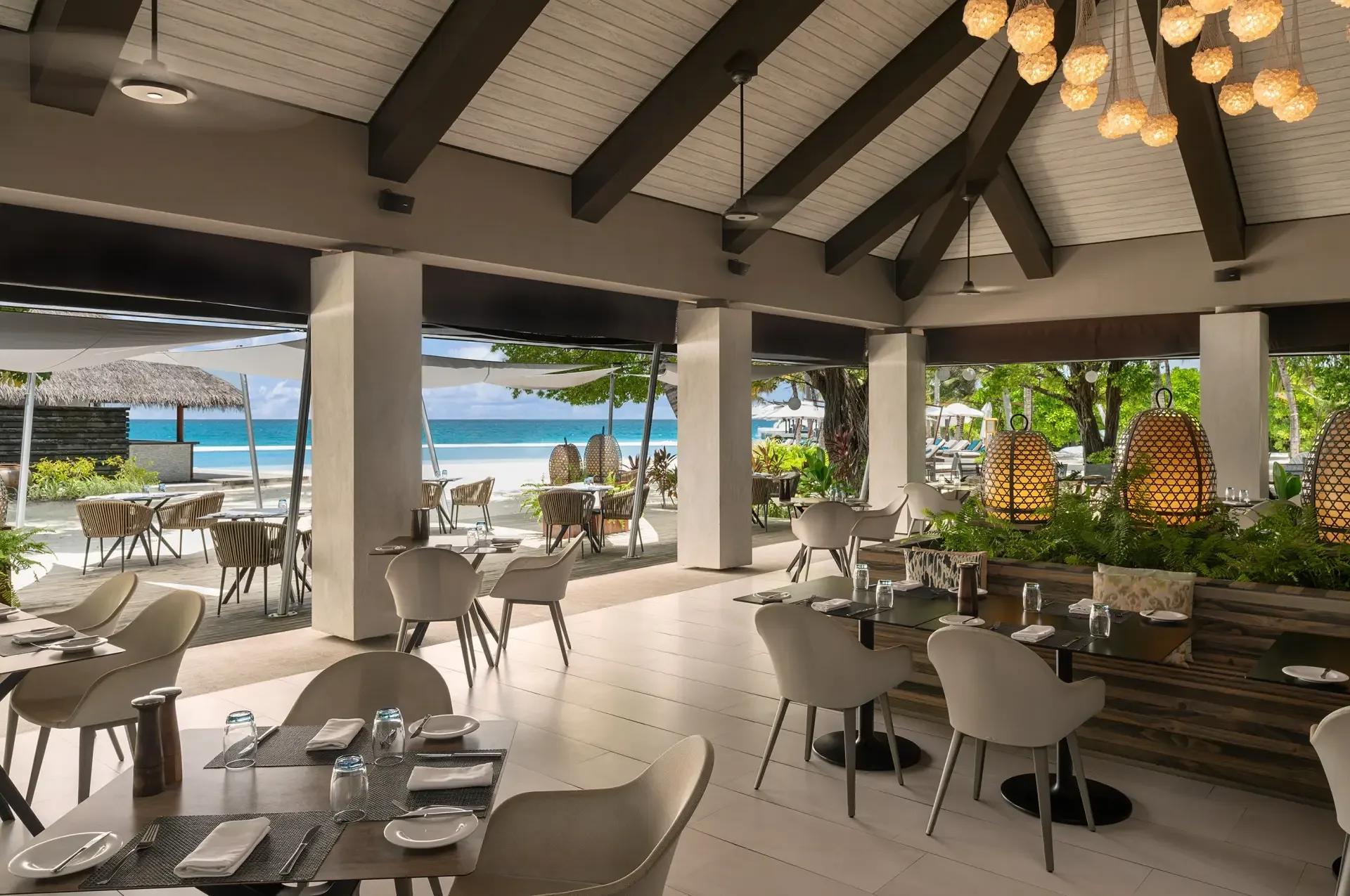 Open-air dining tables at Turquoise, set along the beach with the lagoon visible beyond the palms
