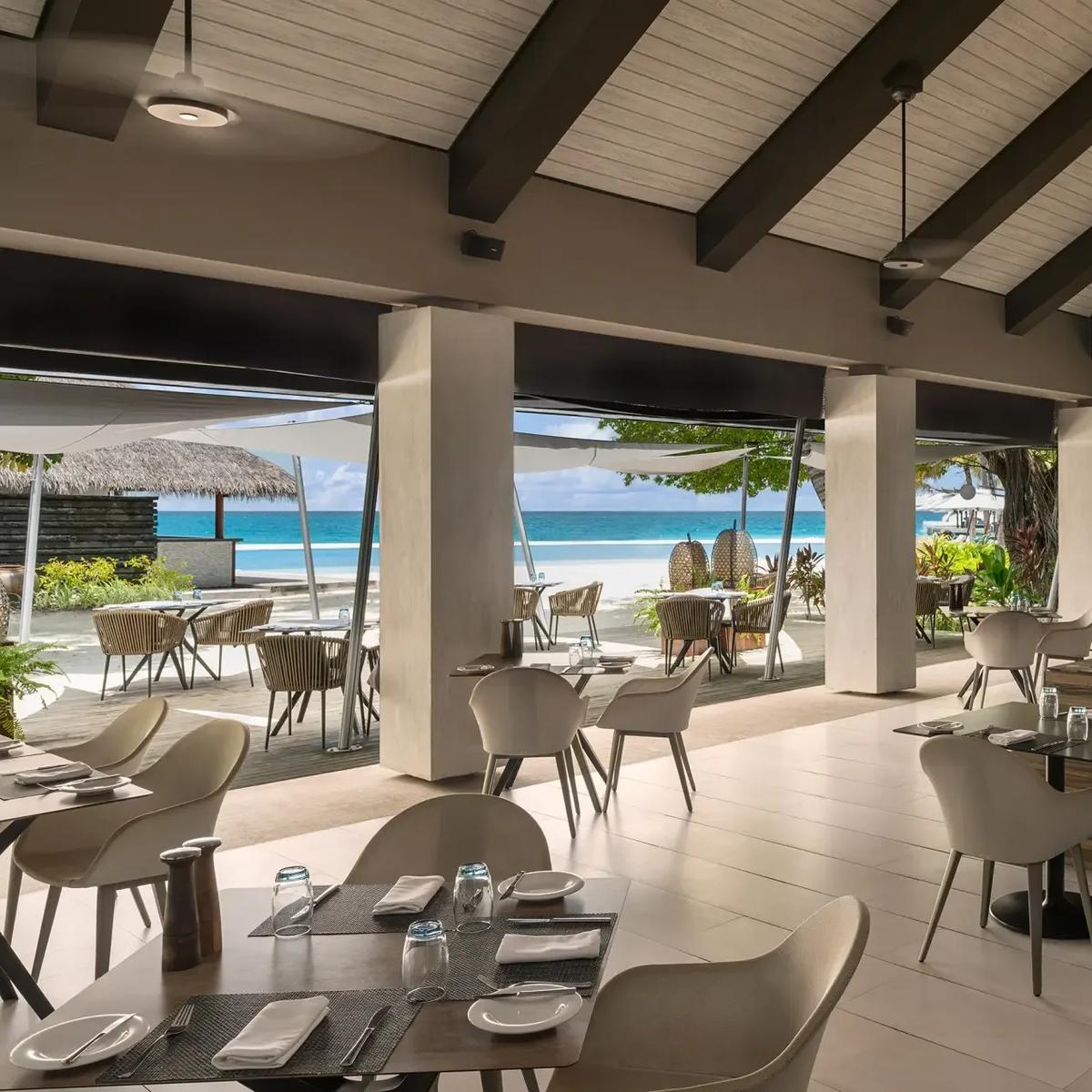 Open-air dining tables at Turquoise, set along the beach with the lagoon visible beyond the palms