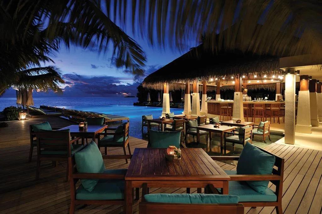 Zero Degree's poolside tables at dusk, the infinity pool and thatched bar lit behind