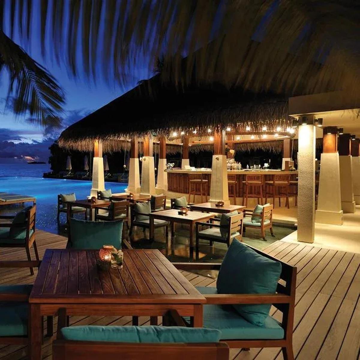 Zero Degree's poolside tables at dusk, the infinity pool and thatched bar lit behind
