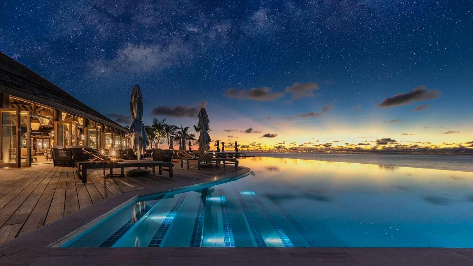 Umi Restaurant's infinity pool deck at dusk, stars appearing overhead as the sky over the lagoon turns orange