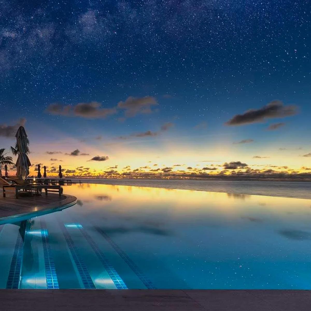 Umi Restaurant's infinity pool deck at dusk, stars appearing overhead as the sky over the lagoon turns orange