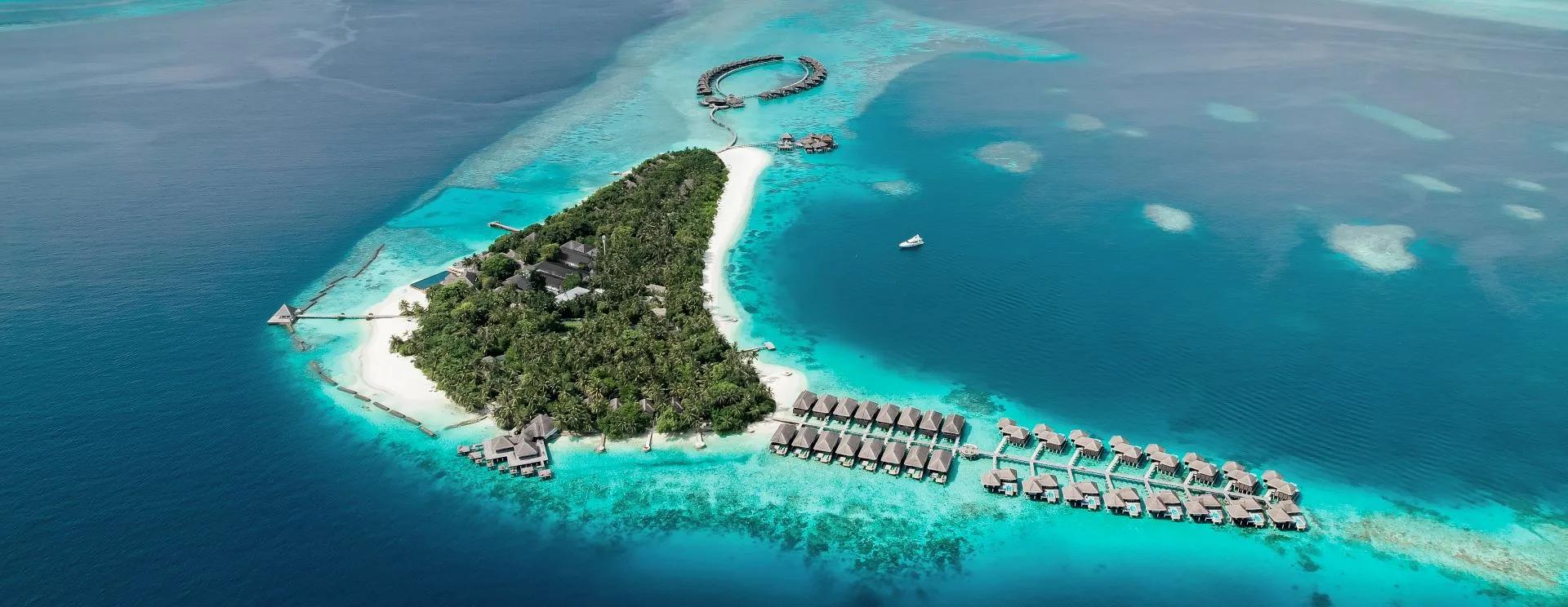 Aerial view of Coco Bodu Hithi's ring-shaped overwater villa cluster and second row of water villas curving into the North Malé Atoll lagoon
